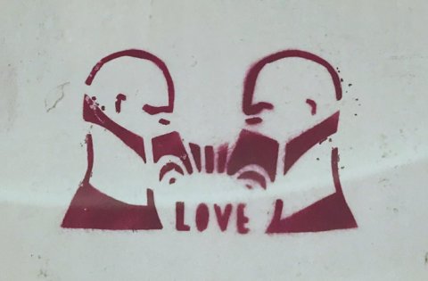 Pochoir sur un mur représentant 2 hommes reliés par des masques à gaz et une inscription "love"